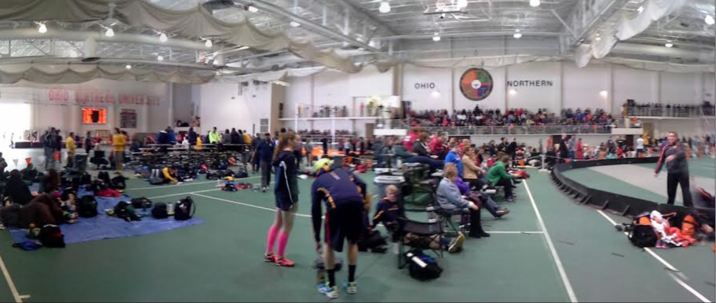 Athletes relax between events on the infield as a large crowd watches on. (Northern Review photo/Dan Knapinski)